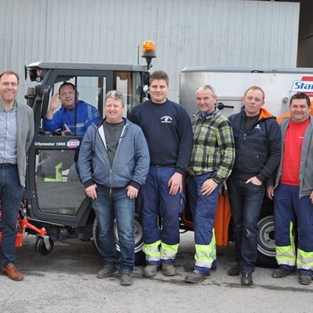 Eine Gruppe von Männern in Arbeitskleidung posiert vor Maschinen mit einem Stängl-Logo, wahrscheinlich an einer Baustelle.