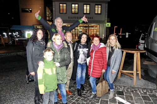 Eine Gruppe von Menschen posiert nachts draußen für ein Foto. Ein Gebäude mit dem Schild 'Raiffeisen Bank' ist im Hintergrund. Die Gruppe besteht aus Erwachsenen und Kindern.