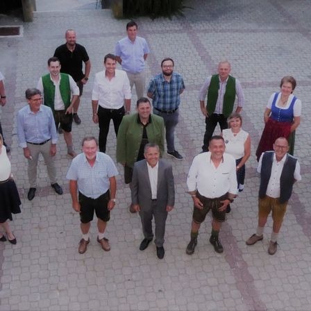 Eine Gruppe von Menschen steht im Kreis, einige in traditioneller Kleidung. Sie lächeln und posieren für ein Foto auf einem gepflasterten Boden.