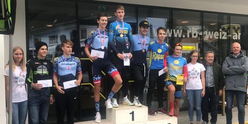 Eine Gruppe von Radfahrern mit Medaillen posiert für ein Foto auf einem Podest vor einem Geschäft.