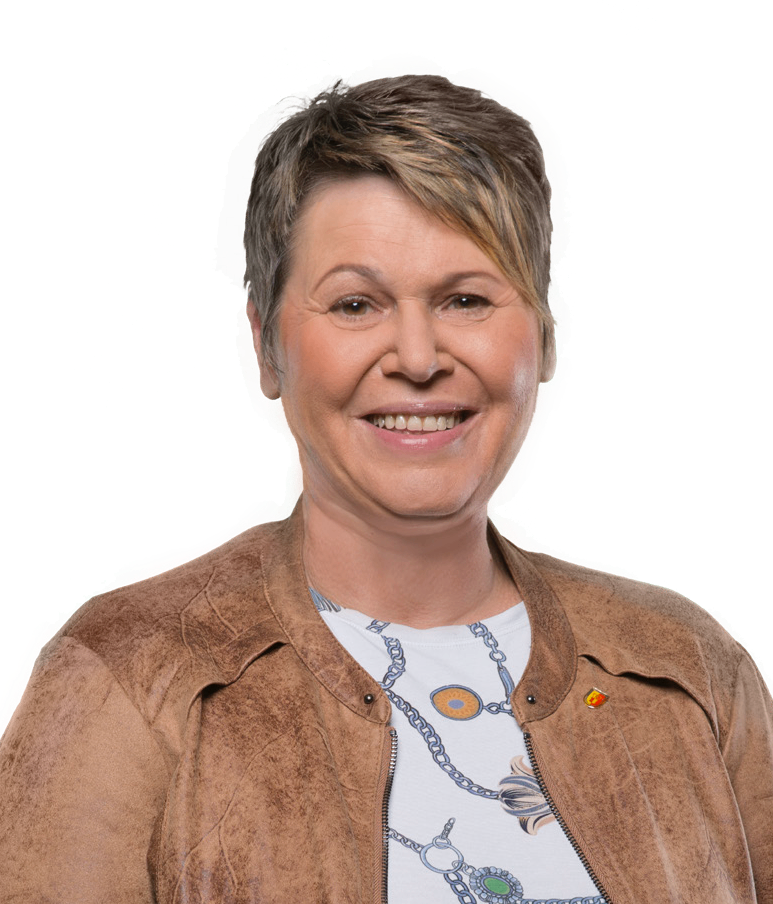 Eine Frau mit kurzen Haaren, die eine braune Jacke mit einem weißen T-Shirt darunter und einer Anstecknadel an ihrer Jacke trägt.