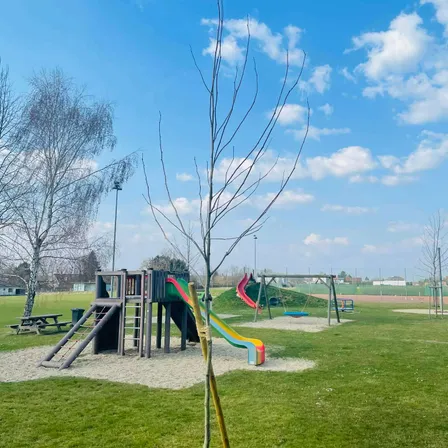 Ein Kinderspielplatz mit Rutschen, Schaukeln und einer Picknick-Bank unter einem blauen Himmel mit Wolken.