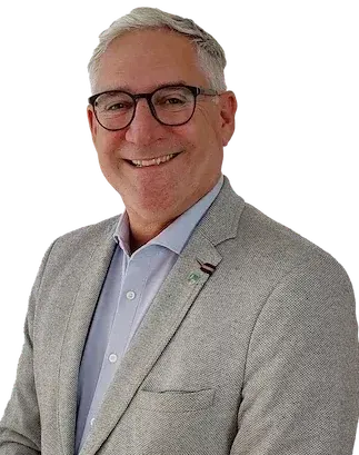 Ein lächelnder Mann mit Brille und heller Jacke posiert für ein Foto vor schwarzem Hintergrund.