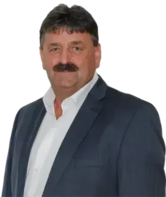 Ein Mann mit Schnurrbart, der einen dunkelblauen Anzug und ein weißes Hemd trägt, posiert für ein Bild vor schwarzem Hintergrund.