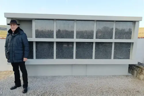 Eine Person steht vor einem modernen Gebäude mit mehreren Glasfenstern, die den Himmel und die umliegenden Bäume reflektieren.