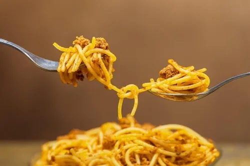 Zwei Gabeln heben Spaghetti mit Fleischsauce hoch, vor einem braunen Hintergrund.