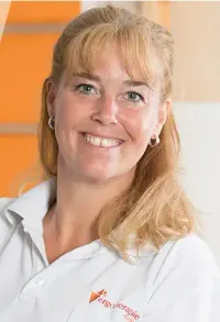 Eine lächelnde Frau mit blonden Haaren und einem weißen Hemd mit einem Logo auf der linken Seite posiert für ein Foto.