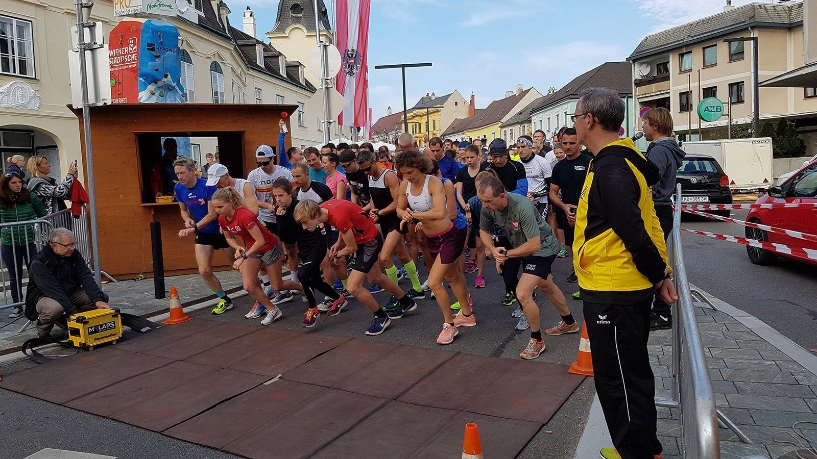 Ein Marathonrennen, Teilnehmer in verschiedenen Farben und Outfits laufen auf der Straße, mit einem Mann vorne und Gebäuden im Hintergrund.