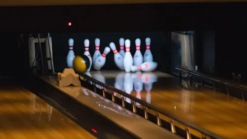 Kegelbahn mit Bowlingkegeln und einem Ball auf der Bahn. Der Ball ist gelb und schwarz.