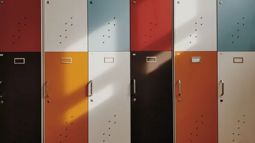 Eine Reihe farbenfroher Schließfächer mit Metallgriffen und Schlössern. Sie sind in verschiedenen Farben wie Orange, Weiß, Blau und Rot lackiert.