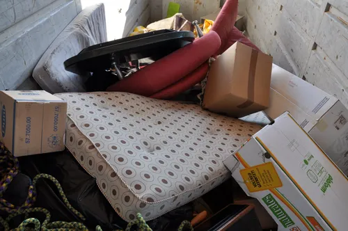 Ein Stapel von Möbeln und Kisten in einem Lagerraum, einschließlich einer gepolsterten Matratze, eines schwarzen Tisches und verschiedener roter und brauner Kissen.
