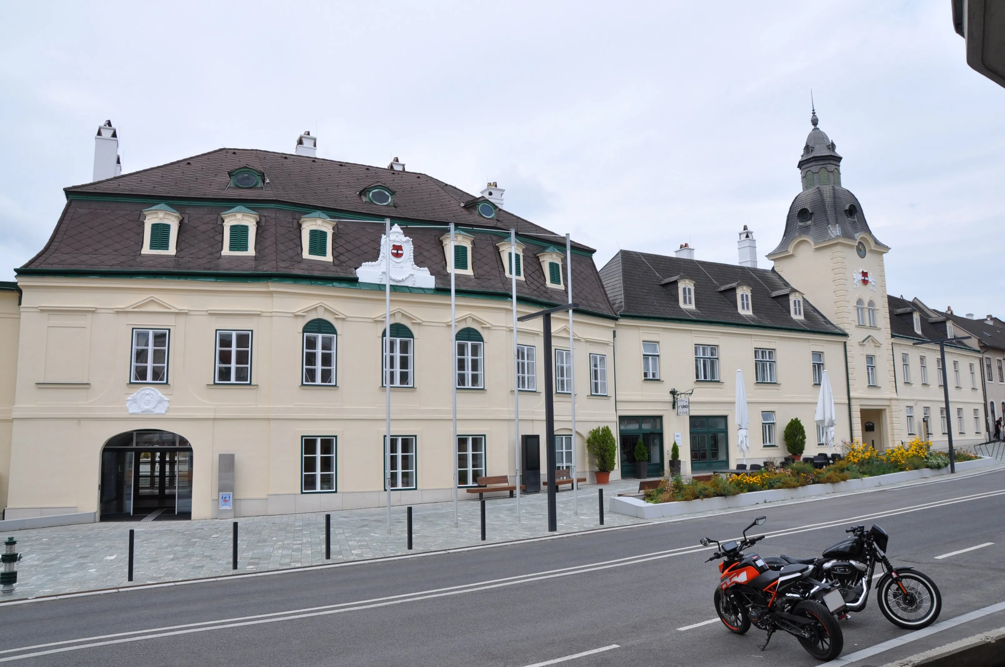 Ein rotes Motorrad ist auf der Straßenseite vor einem großen Gebäude geparkt.
