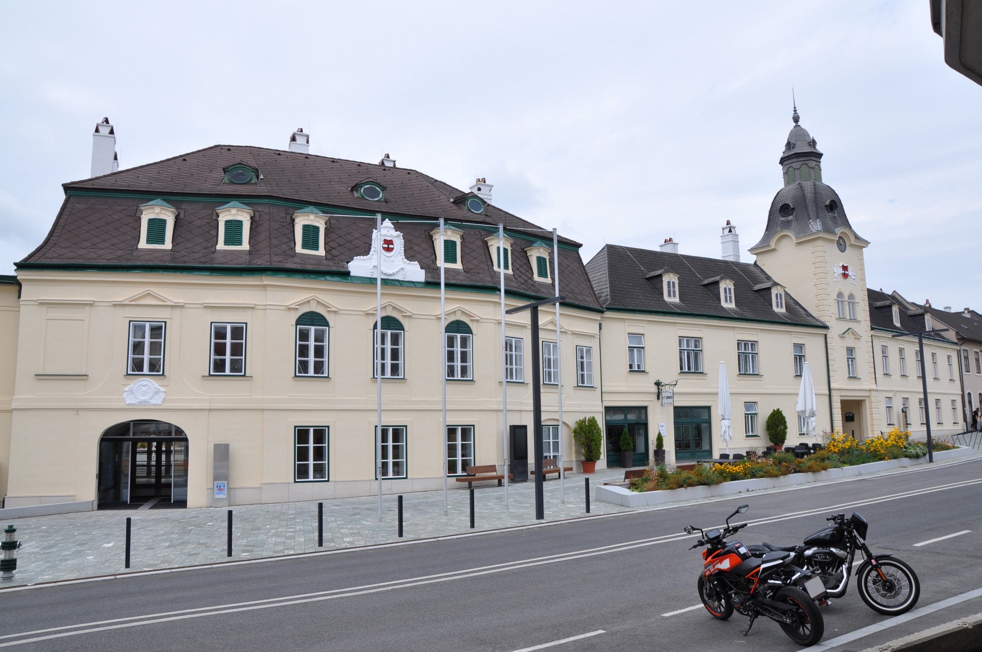 Ein beiges Gebäude mit vielen Fenstern und einer Flagge steht in der Nähe einer Straße mit geparkten Motorrädern.