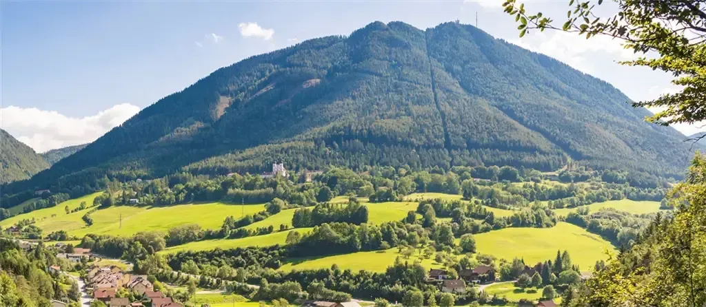 Ein Berg mit grünen Feldern und Häusern in einem Tal unter einem blauen Himmel mit Wolken.