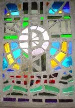 Ein Mosaik aus verschiedenen farbigen Glasstücken, mit einem zentralen Spiralmuster, das von hinten beleuchtet wird.