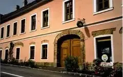Ein rosa Gebäude mit mehreren Fenstern und einer Holztür an einer Straße mit Pflanzen und einer weißen Linie auf der Seite.
