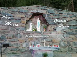 Ein Steinaltar mit einer Statue der Jungfrau Maria und der Inschrift 'Ego sum Immaculata Conceptio'. Kleine Kerzen sind um den Altar herum platziert. Die Worte 'Gratia Plena' sind oben auf der Wand.