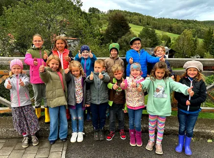Eine Gruppe von Kindern und Jugendlichen posiert für ein Foto in einer ländlichen Umgebung mit einer Kulisse aus Hügeln und Bäumen. Sie alle lächeln und geben Daumen hoch.