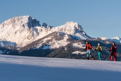 Drei Personen langlaufen auf einem verschneiten Berg mit klarem blauem Himmel.