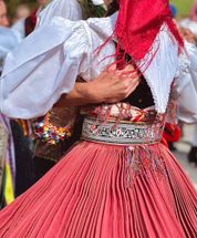 Eine Frau in einem traditionellen roten Kleid und einer weißen Bluse mit einem roten Schal tanzt mit einem Mann in einem weißen Hemd und einem roten Schal.
