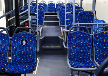 Ein leerer Businnenraum mit blauen Sitzen, einem Rollstuhlfahrer-Schild und einer Treppe, die zum Fahrerbereich führt.