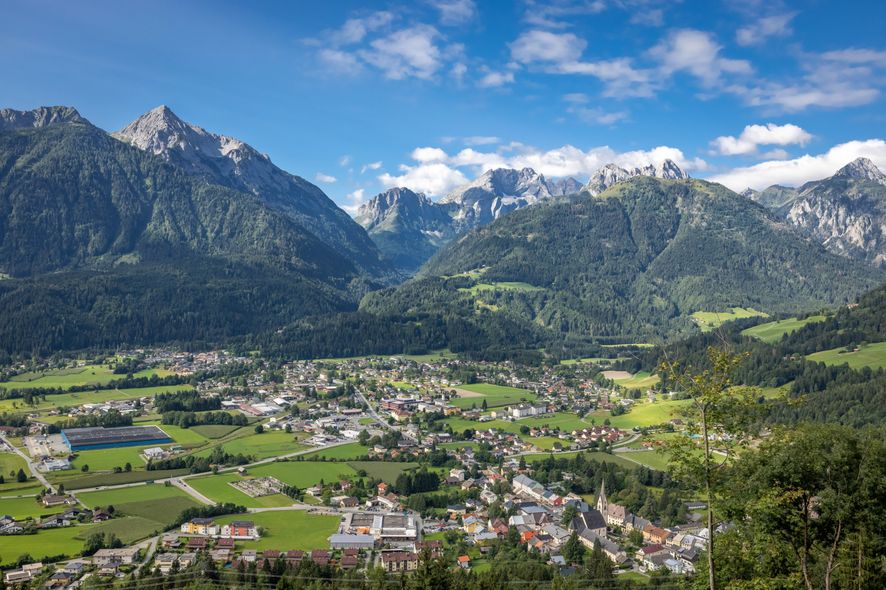 Luftaufnahme einer kleinen Stadt zwischen Bergen. Die Stadt ist von üppigen grünen Feldern und Bäumen umgeben.