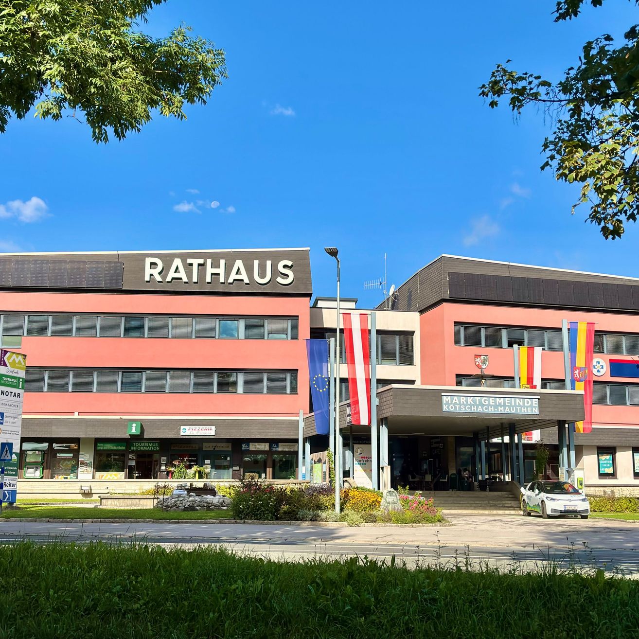 Das Rathaus-Gebäude ist ein großes, rot-weißes Gebäude mit einem großen Schild, auf dem Rathaus steht. Es hat mehrere Fenster und Flaggen davor.