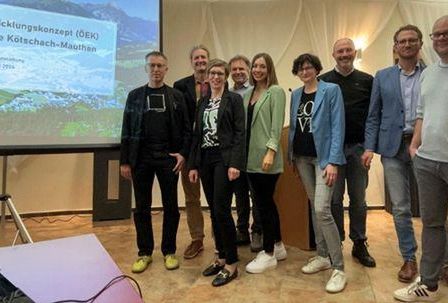 Gruppe von Menschen vor einer Projektionsleinwand mit Text auf Deutsch über ein Entwicklungskonzept für Kotschach-Mauthen.