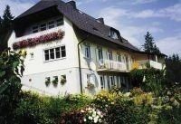 Ein weißes Haus mit schwarzem Dach und vielen Fenstern, umgeben von einem Garten mit Blumen und Pflanzen.