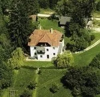 Ein Luftbild eines großen weißen Hauses mit einem braunen Dach, umgeben von saftigem grünem Laub und Gras in einer ländlichen Gegend.