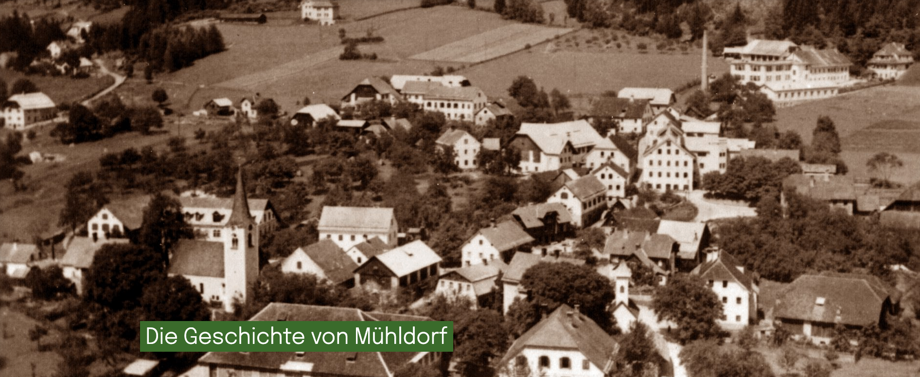 Eine historische Luftaufnahme des Ortes Mühldorf mit vielen traditionellen Häusern und Gebäuden, umgeben von viel Grün.