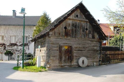 Ein altes Holzhaus mit einer Tür und einem Rad davor befindet sich am Straßenrand. Eine Straßenlaterne und ein Zaun befinden sich am Straßenrand.