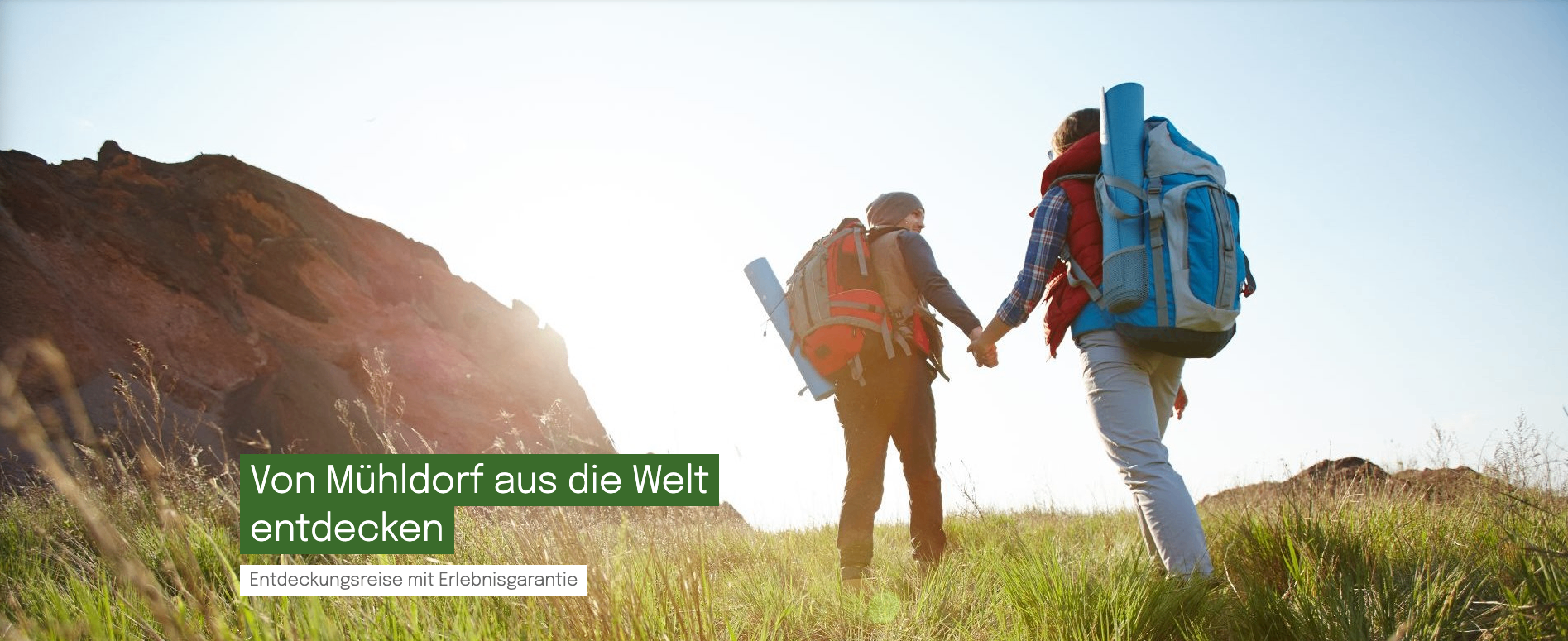 Zwei Menschen halten Händchen und gehen auf einem Feld. Einer trägt einen Rucksack und eine Weste, der andere einen Rucksack. Heller Sonnenschein und ein Berg im Hintergrund. Der Text lautet 'aus die Welt'.