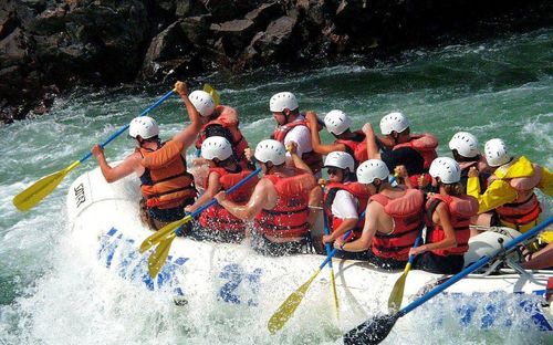 Eine Gruppe von Menschen treibt auf einem Fluss mit felsigen Klippen. Sie tragen alle Rettungswesten und Helme und halten Paddel.