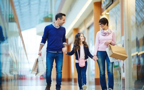 Eine lächelnde dreiköpfige Familie, ein Mann, eine Frau und ein junges Mädchen, gehen Hand in Hand und mit Einkaufstüten in einem Einkaufszentrum.