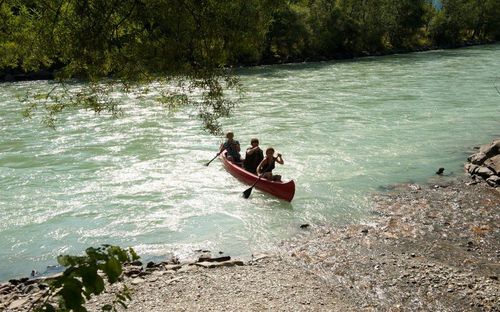Drei Personen sitzen in einem roten Kanu auf einem Fluss. Sie paddeln, und der Fluss ist von Bäumen umgeben.