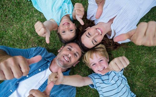 Eine vierköpfige Familie liegt auf dem Gras und zeigt alle Daumen hoch. Die Frau und die beiden Kinder lächeln, während der Mann in die Kamera schaut.