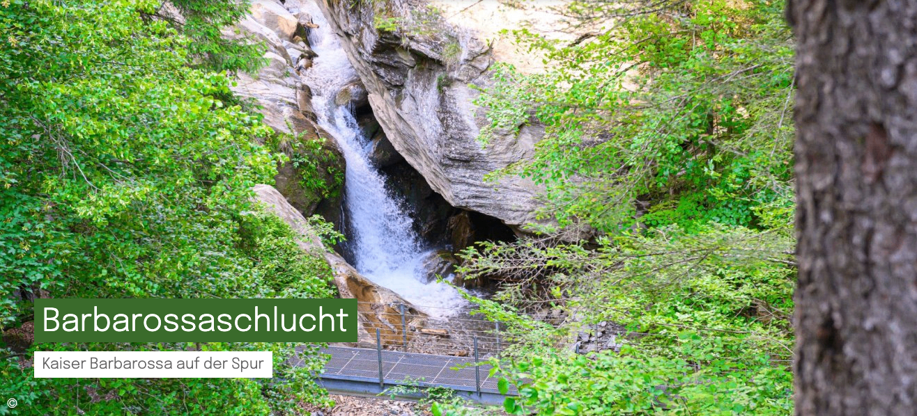 Ein Wasserfall stürzt an den Felsen hinunter, umgeben von üppigem Grün und einem Metallgeländer zur Sicherheit.