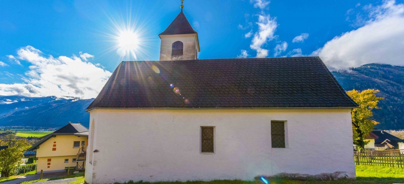 Eine weiße Kirche mit schwarzem Dach und einem Turm glänzt unter einem klaren blauen Himmel mit einer strahlenden Sonne.
