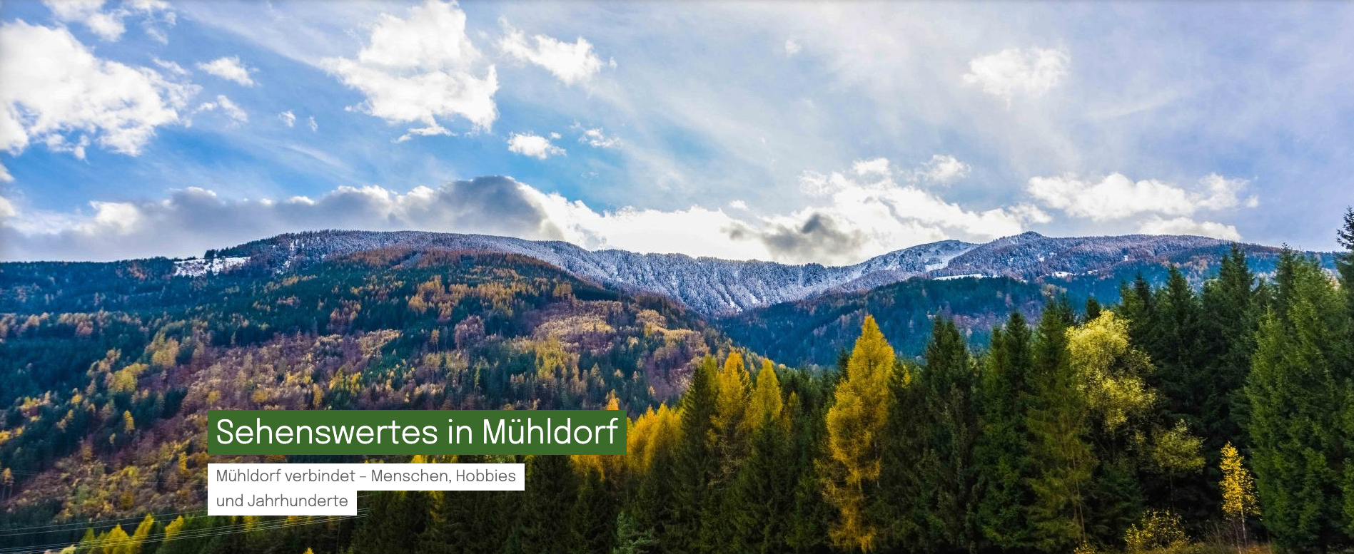 Ein Panoramablick auf verschneite Berge und grüne Bäume. Der Himmel ist teilweise bewölkt. Der Text lautet 'es in Mühldorf'.
