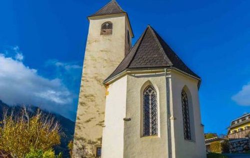 Eine Kirche steht unter einem blauen Himmel mit einem Turm und einem Glockenturm, in der Nähe eines Berges.