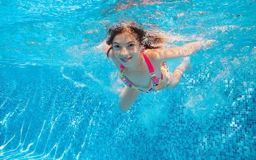 Ein junges Mädchen in einem blumigen Badeanzug schwimmt fröhlich unter dem klaren blauen Wasser in einem Pool.