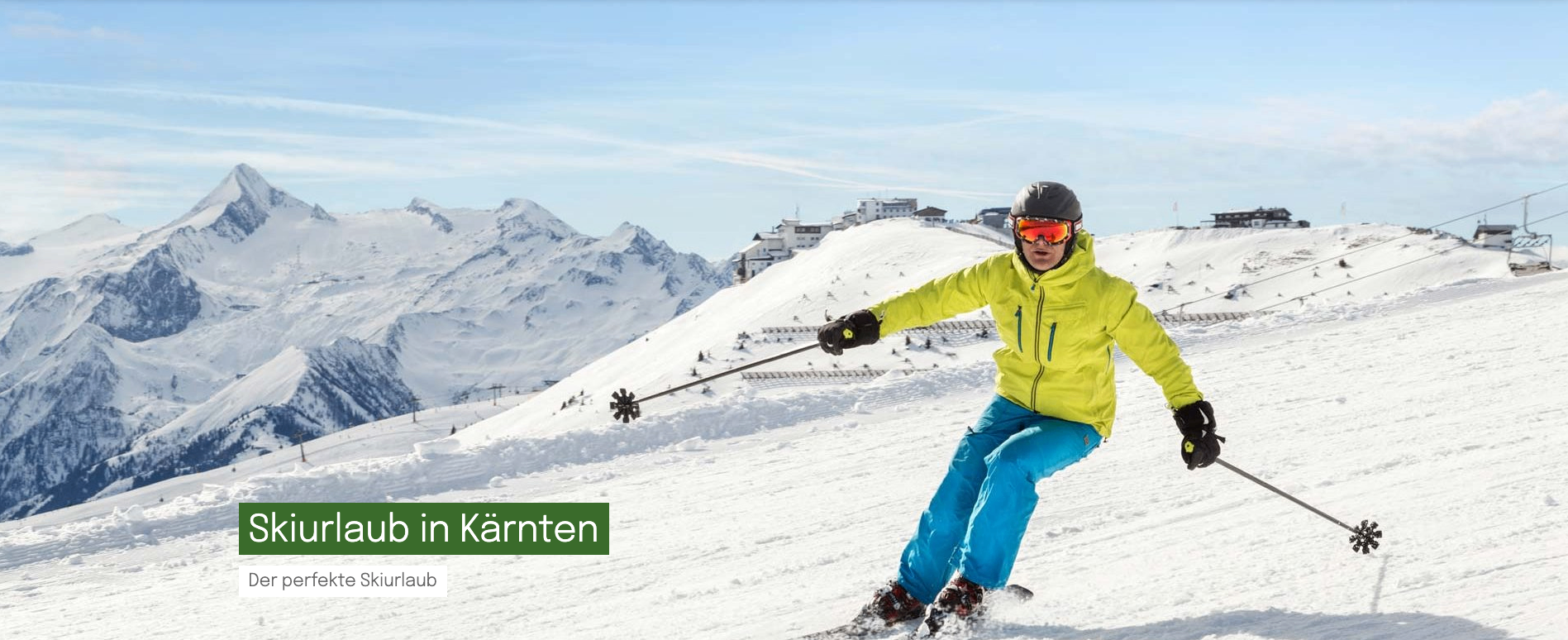 Ein Skifahrer mit gelber Jacke, blauer Hose und roten Skibrille fährt mit einem Skistock den schneebedeckten Berg hinunter. Im Hintergrund sind Berge und Gebäude zu sehen.