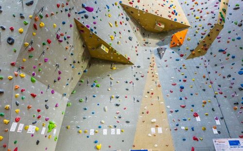 Eine Kletterwand mit verschiedenen farbigen Griffen und Haltepunkten. Die Wand hat mehrere Ebenen mit Dreiecken und Quadraten. Kletterer können verschiedene Wege zum Gipfel sehen.