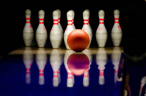 Bowlingkugel vor Bowling Pins, reflektiert auf der blauen Bahn.