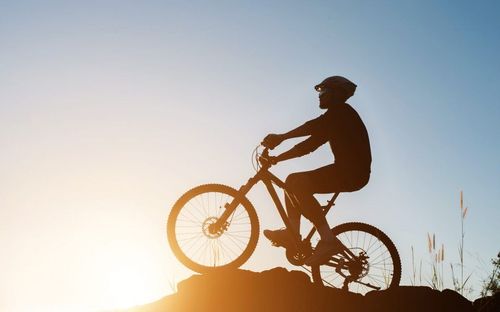 Eine Person fährt mit einem Mountainbike über einen felsigen Hügel bei Sonnenuntergang. Der Fahrer trägt einen Helm und Fahrradhandschuhe.