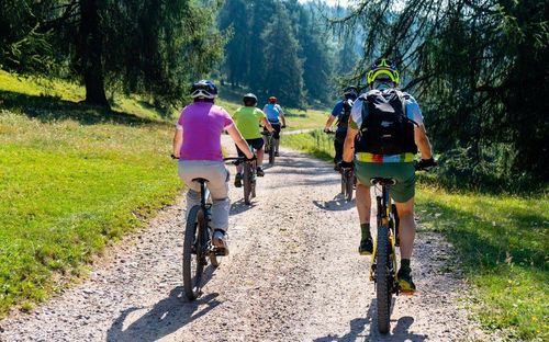 Eine Gruppe von Radfahrern mit Helmen fährt auf einem Schotterweg, umgeben von Bäumen. Sie genießen eine Fahrt im Wald.