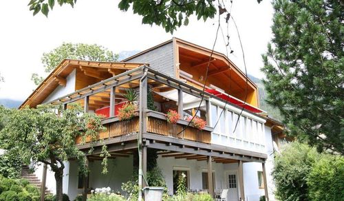 Ein zweistöckiges Haus mit Balkon und rotem Vordach. Das Haus hat Glasfenster, eine Terrasse mit Holzgeländer und einen Garten.
