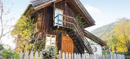 Ein altes Holzhaus mit einer Holztür und einem Balkon mit einem Glasfenster, umgeben von einem weißen Zaun und Kletterpflanzen.