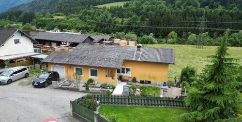 Ein Luftbild eines gelben Hauses mit einem grauen Dach, umgeben von Bäumen und einem grünen Feld. Ein Auto ist auf der Einfahrt geparkt.